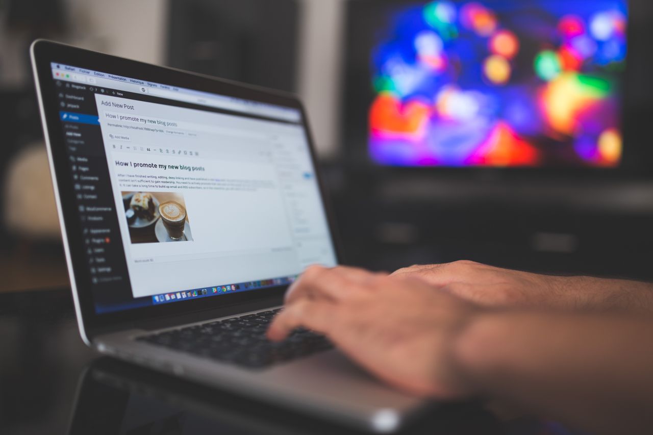 about-us Hands typing on a laptop with a blog post visible, cozy indoor setting with colorful screen in background.